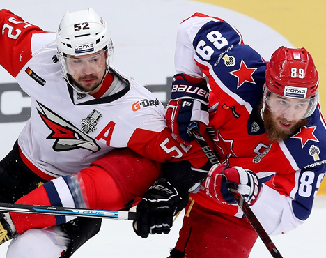 Хоккейный матч: два игрока в борьбе за шайбу. Один в форме красно-белого клуба с номером 52, другой в красно-синей форме с номером 89. Эмоциональное противостояние на льду